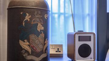 A decorative urn with intricate designs next to a modern speaker on a wooden table.