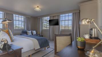 Une chambre d’hôtel avec un grand lit, un bureau avec une lampe, une télévision et une vue sur l’extérieur grâce à de grandes fenêtres.