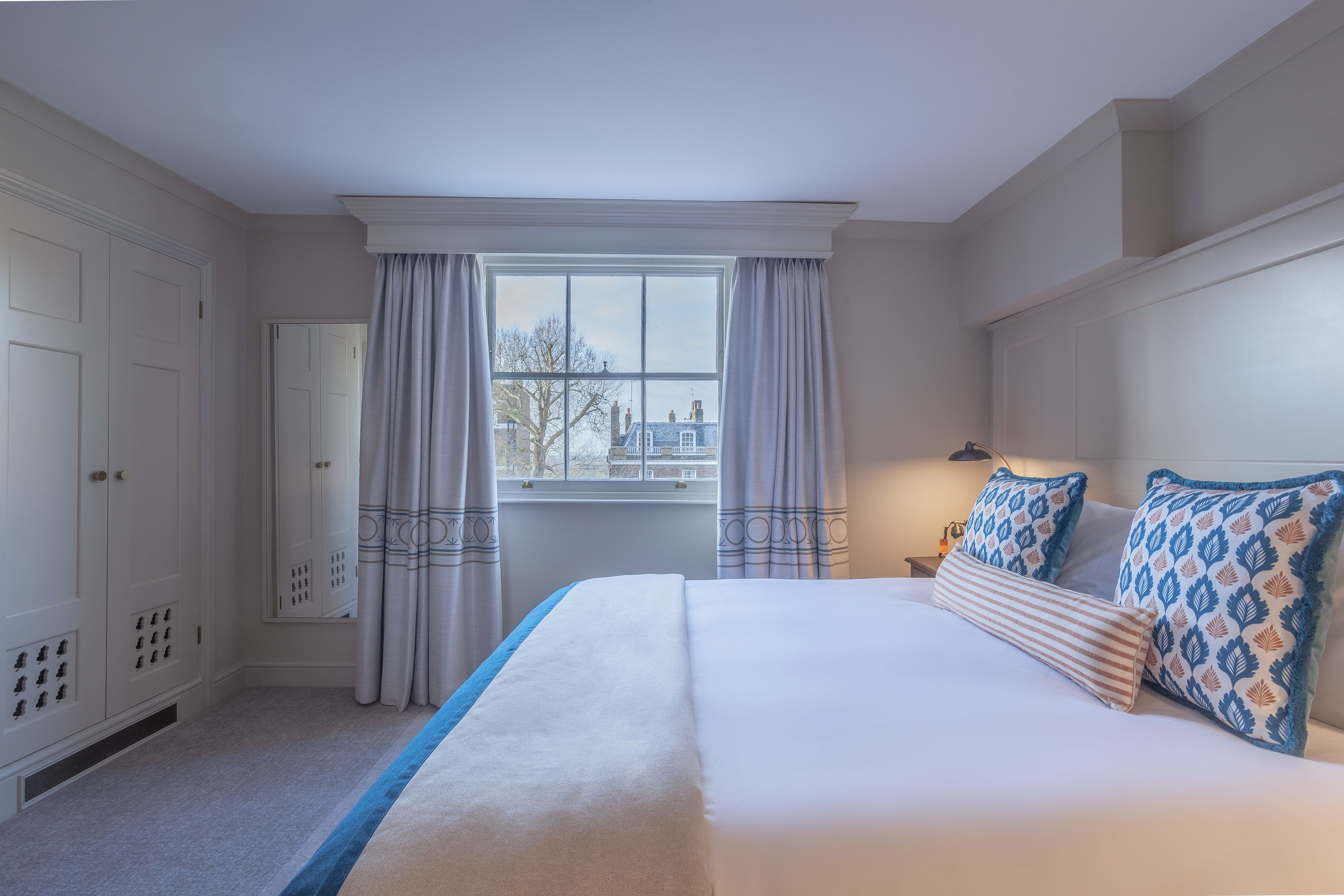 Ein Schlafzimmer mit einem großen Bett, einem Fenster mit Vorhängen, einem Kleiderschrank und einem Nachttisch mit Lampe.
