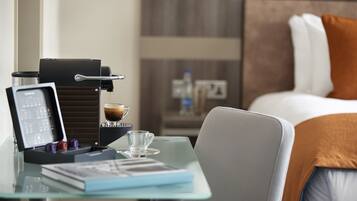 A hotel room with a bed, a glass table with a coffee machine, a laptop, and a book.