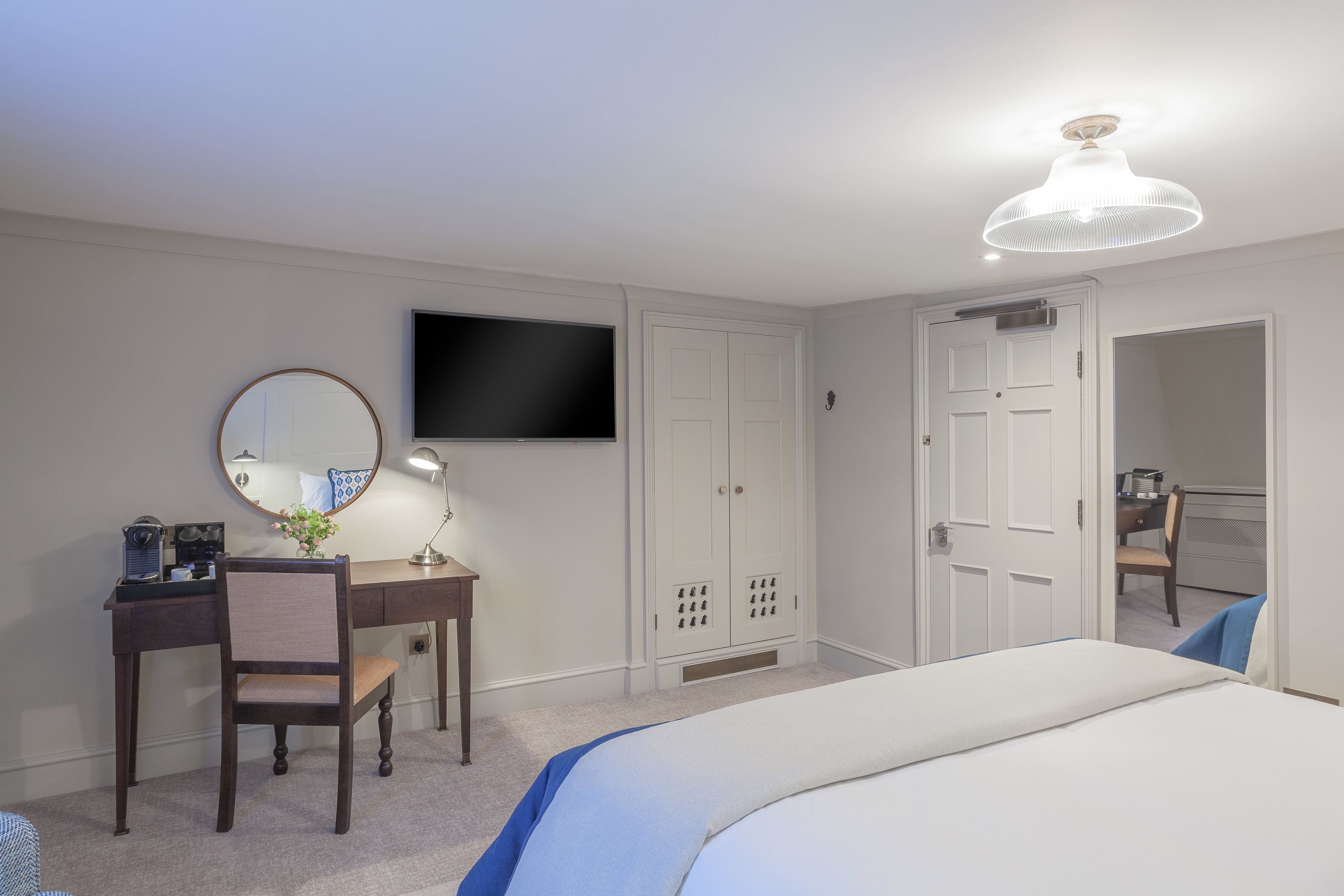 A hotel room with a bed, a desk with a chair, a television, and a wardrobe.