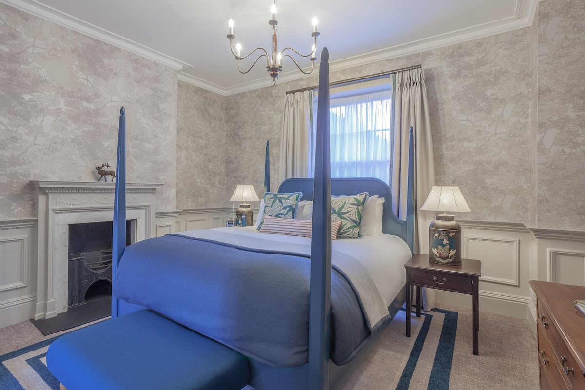 A bedroom with a four-poster bed, a fireplace, and a chandelier.