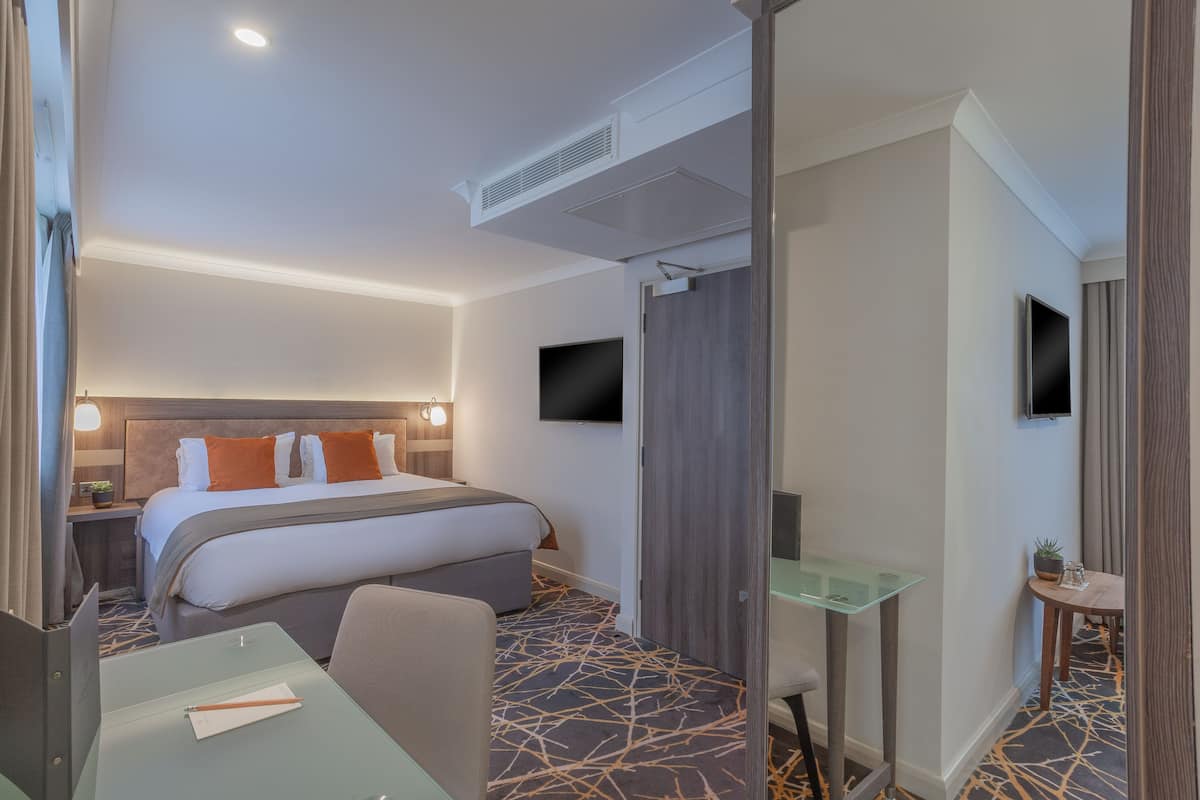 A hotel room with a bed, desk, chair, TV, and a small table with a plant.