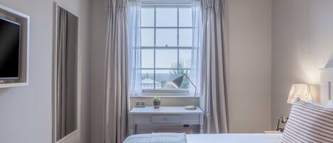 Habitación de hotel con cama, escritorio con lámpara, televisión y ventana con cortinas.