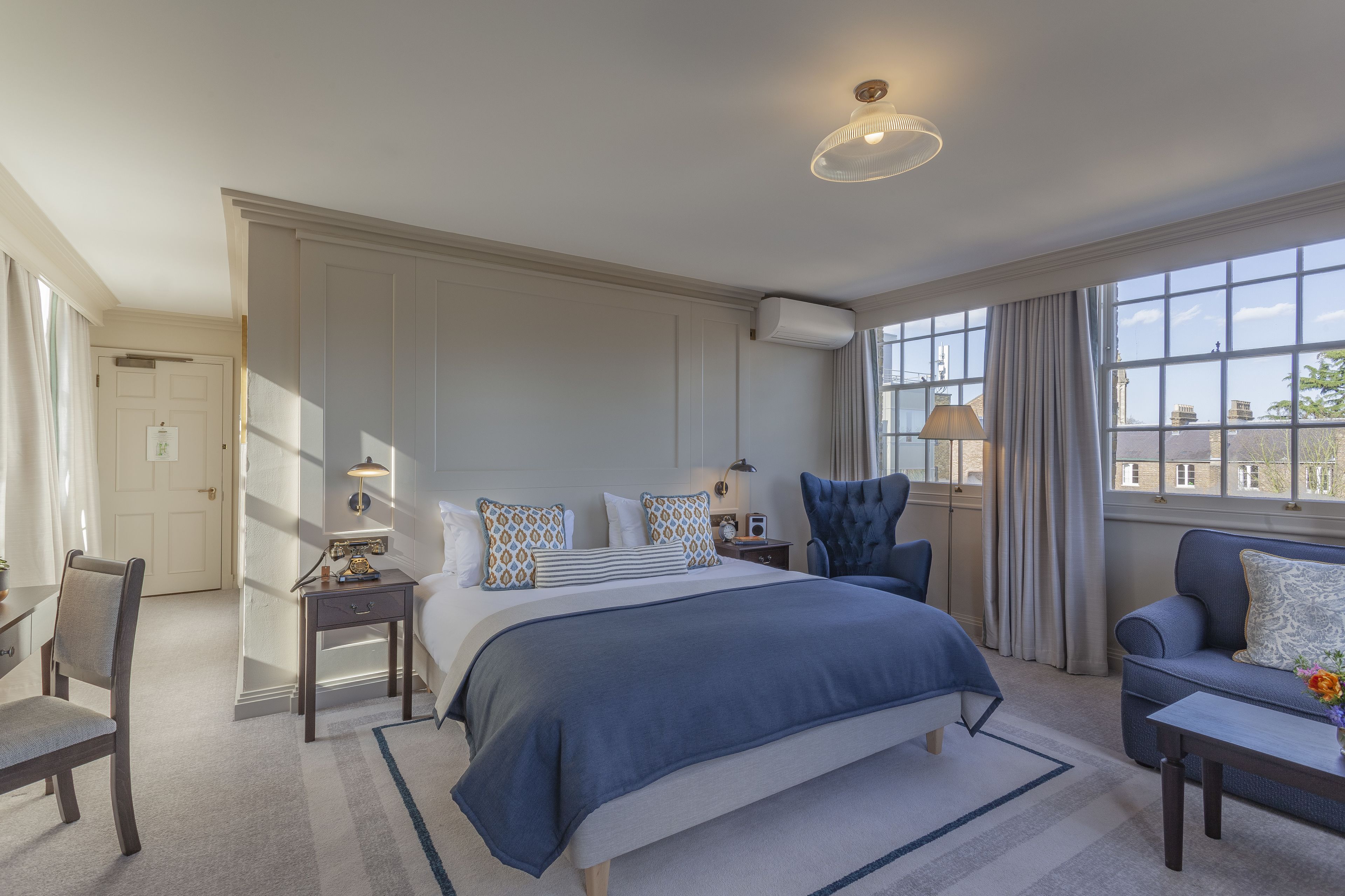 A bedroom with a large bed, a chair, a desk, and a window with curtains.