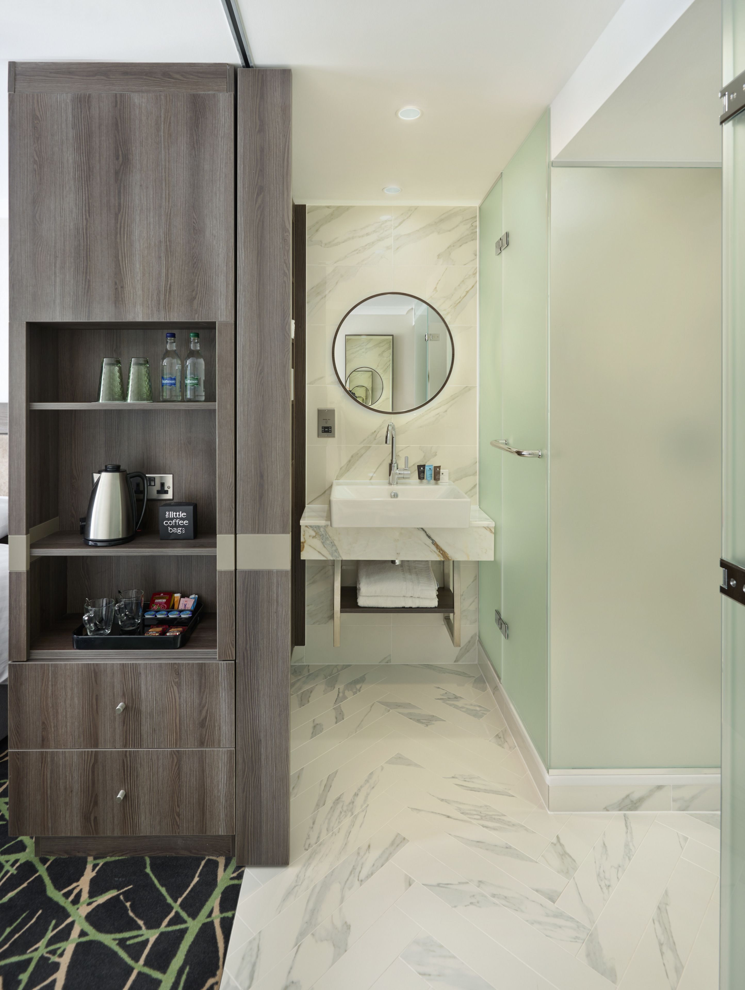 A modern bathroom with a marble sink, a round mirror, and a built-in cabinet with toiletries.