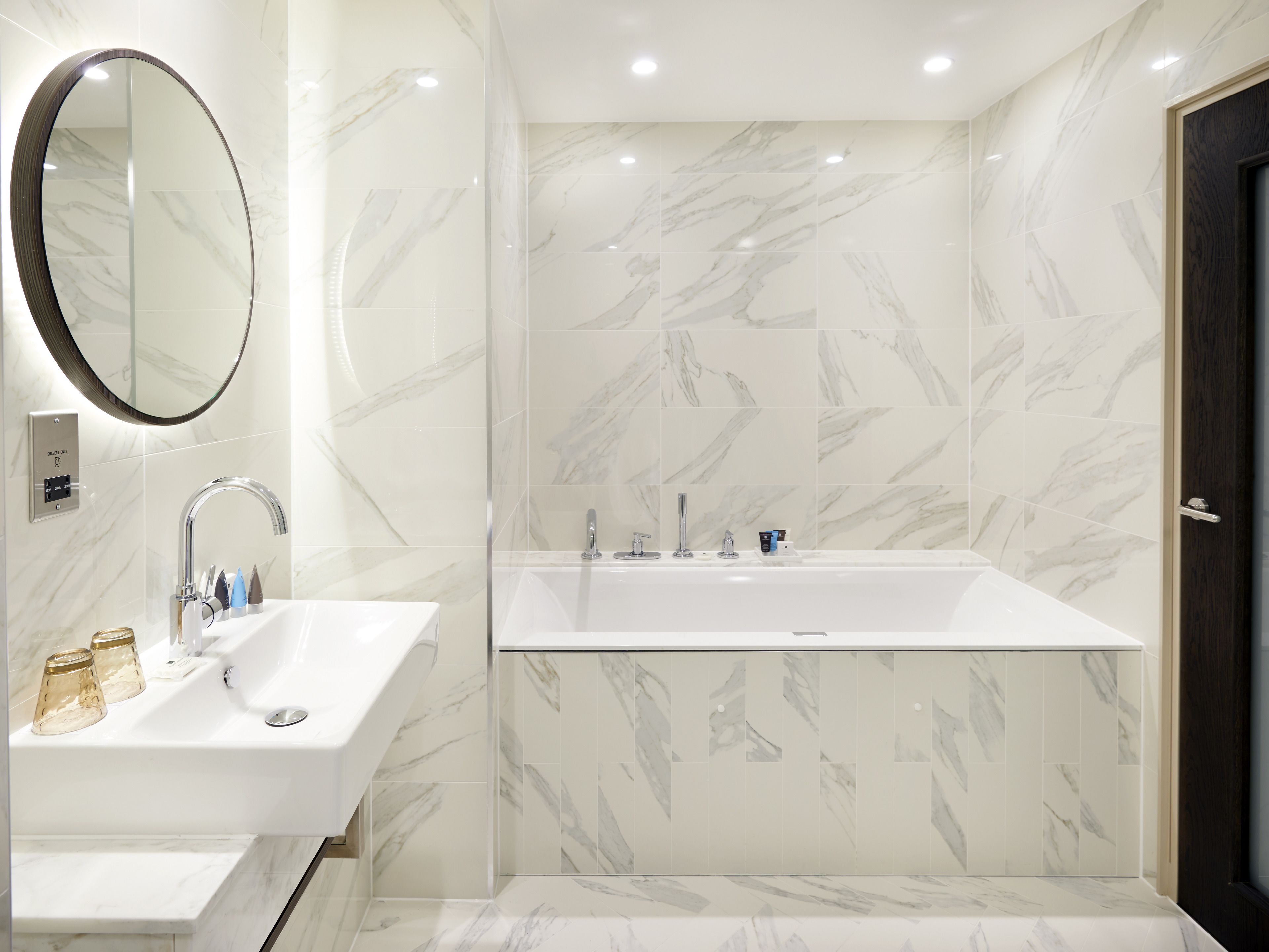 A modern bathroom with a large mirror, a sink, and a bathtub.