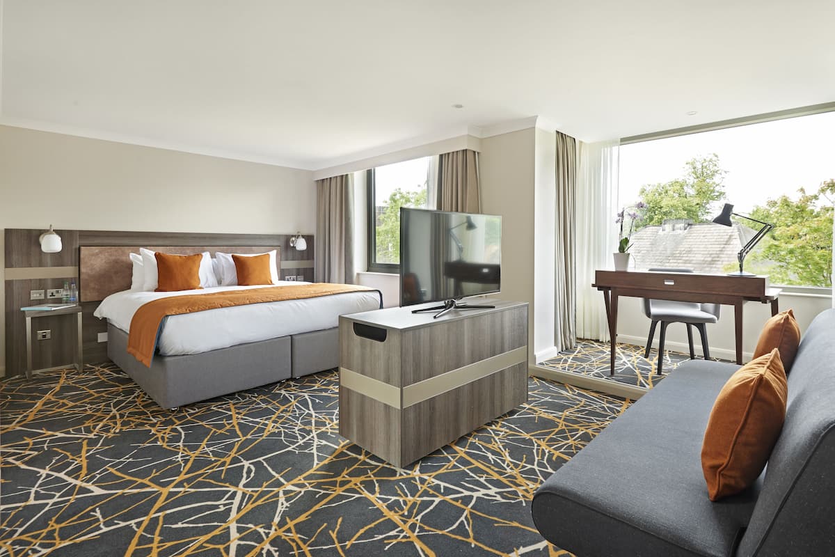 A hotel room with a bed, a desk, a TV, and a sofa.