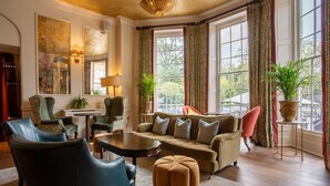 A well-lit living room with a sofa, chairs, a coffee table, and large windows with curtains. - Richmond Hill Hotel (Richmond)