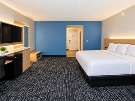 Habitación de hotel con cama, escritorio con computadora, televisor y una pequeña planta.