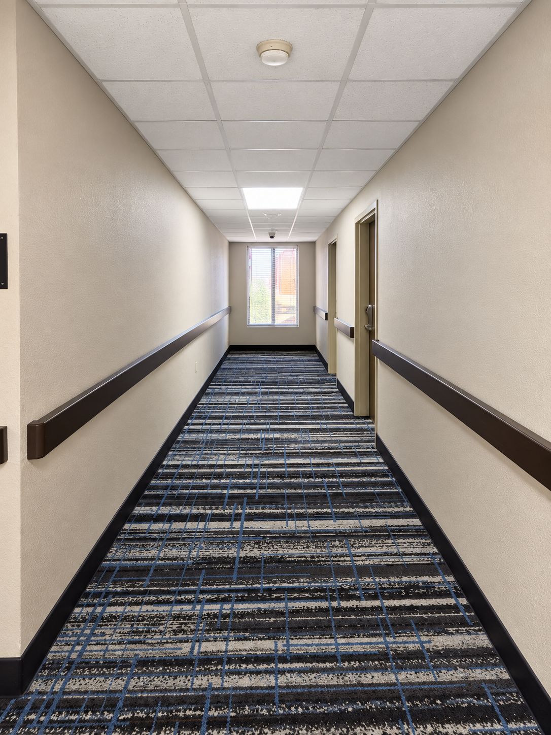 A hotel corridor with a patterned carpet, a ceiling light, and a door on the right.