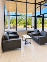 Un área de estar moderna en el interior, con ventanas amplias, piso de baldosas y vista al exterior.
