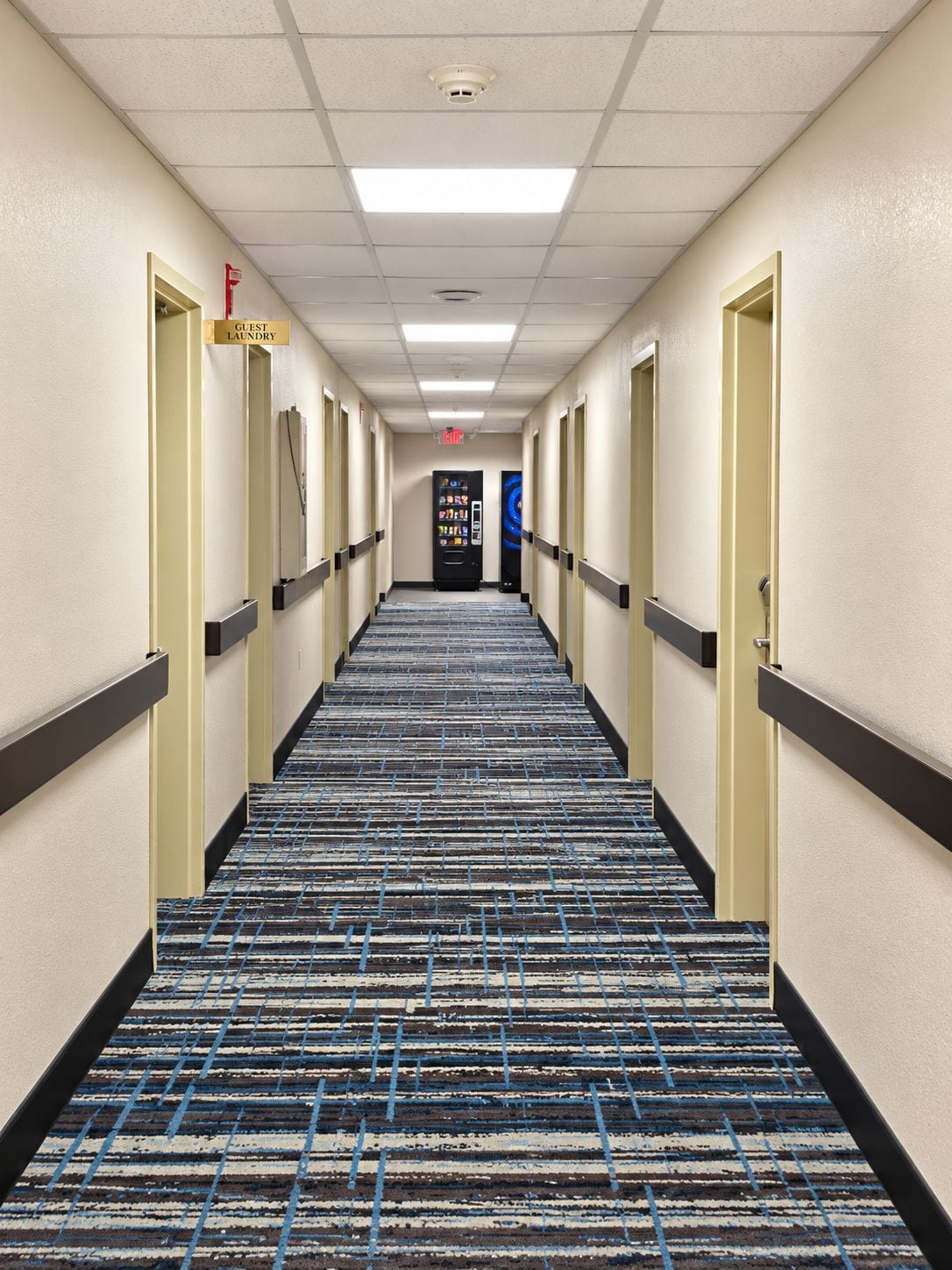 A hotel corridor with a carpeted floor, doors on both sides, and a vending machine in the center.