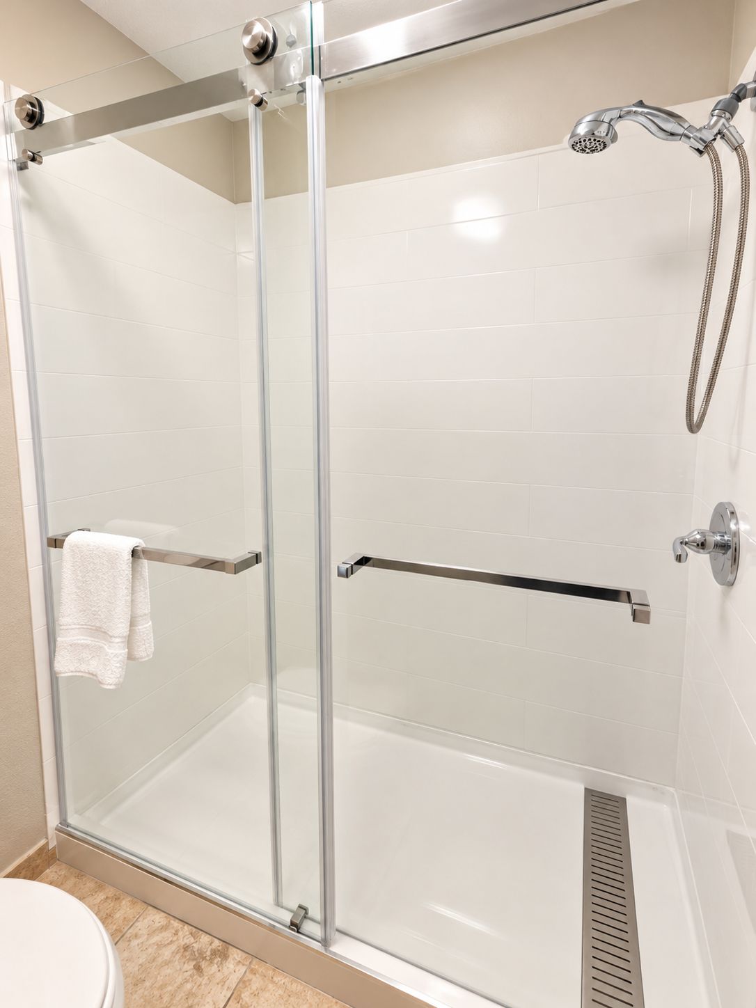 A glass-enclosed shower stall with a handheld showerhead and a towel rack.