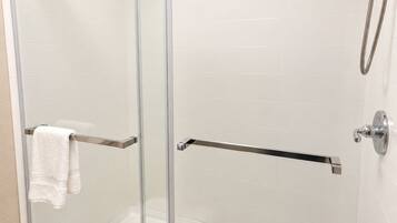 A glass-enclosed shower stall with a handheld showerhead and a towel rack.