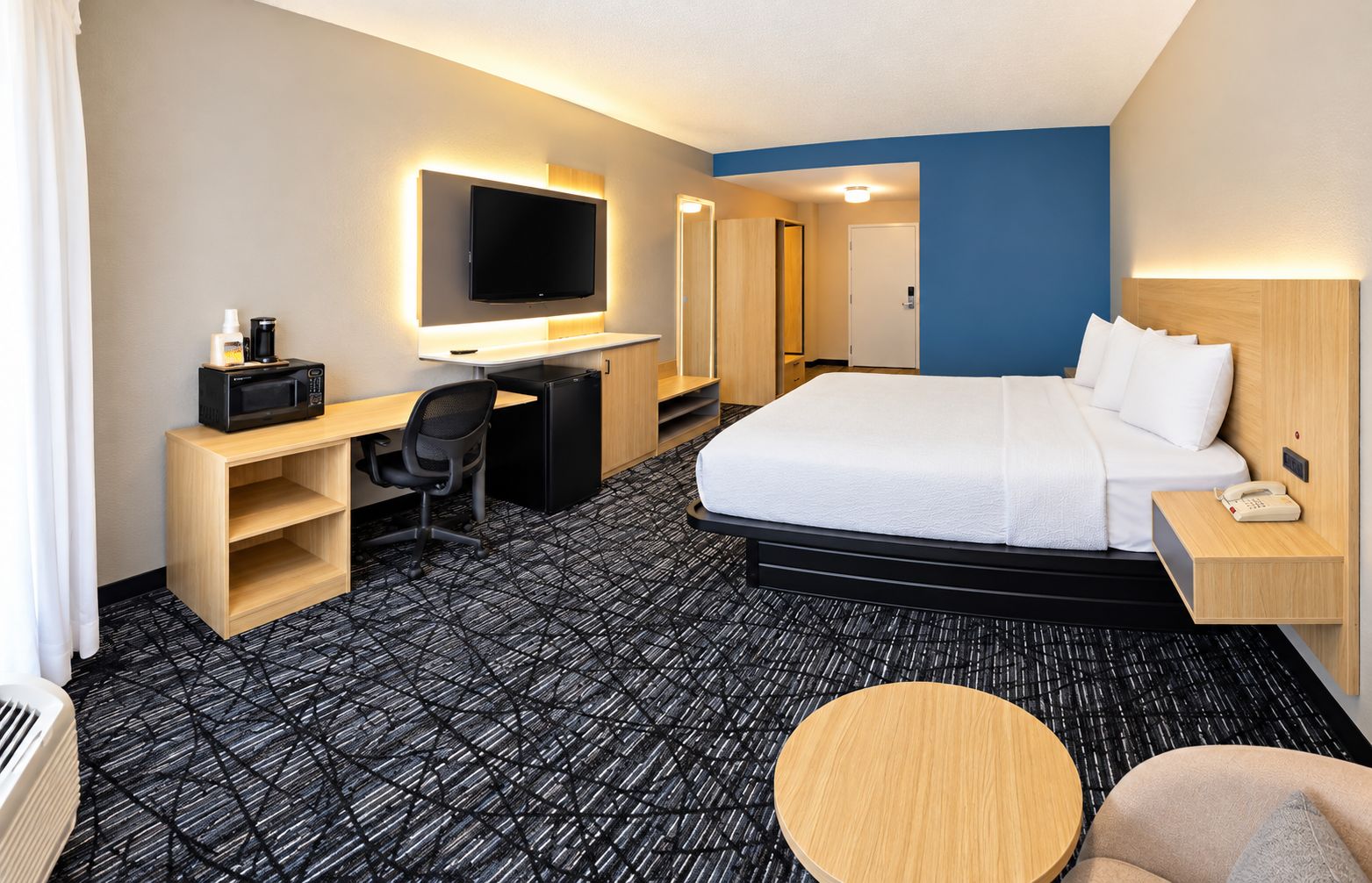 A hotel room with a bed, desk, chair, television, and a small round table.