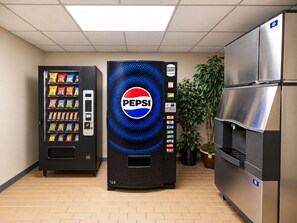 Màquina expenedora amb logotip de Pepsi, un refrigerador i una planta en test amb ambient interior.