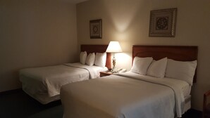 A hotel room with two single beds, a bedside table with a lamp, and two framed pictures on the wall. - Gold Vault Inn (Radcliff)