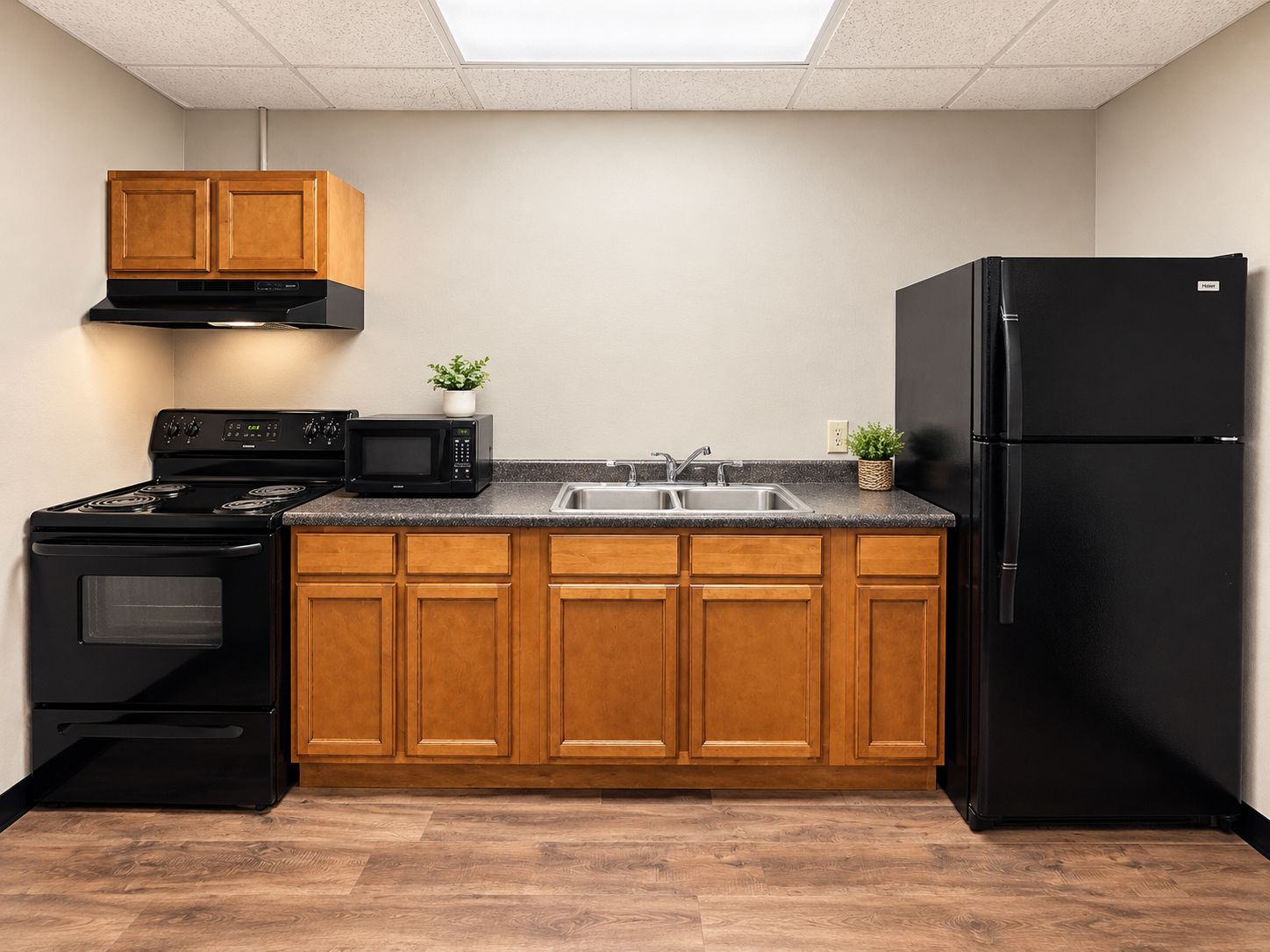 A kitchen with wooden cabinets, a black stove, a microwave, a sink, and a black refrigerator.