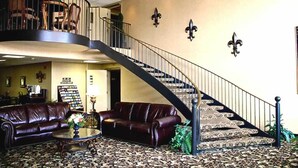 A spacious lobby with a curved staircase, leather sofas, a coffee table, and a bookshelf. - Gold Vault Inn (Radcliff)