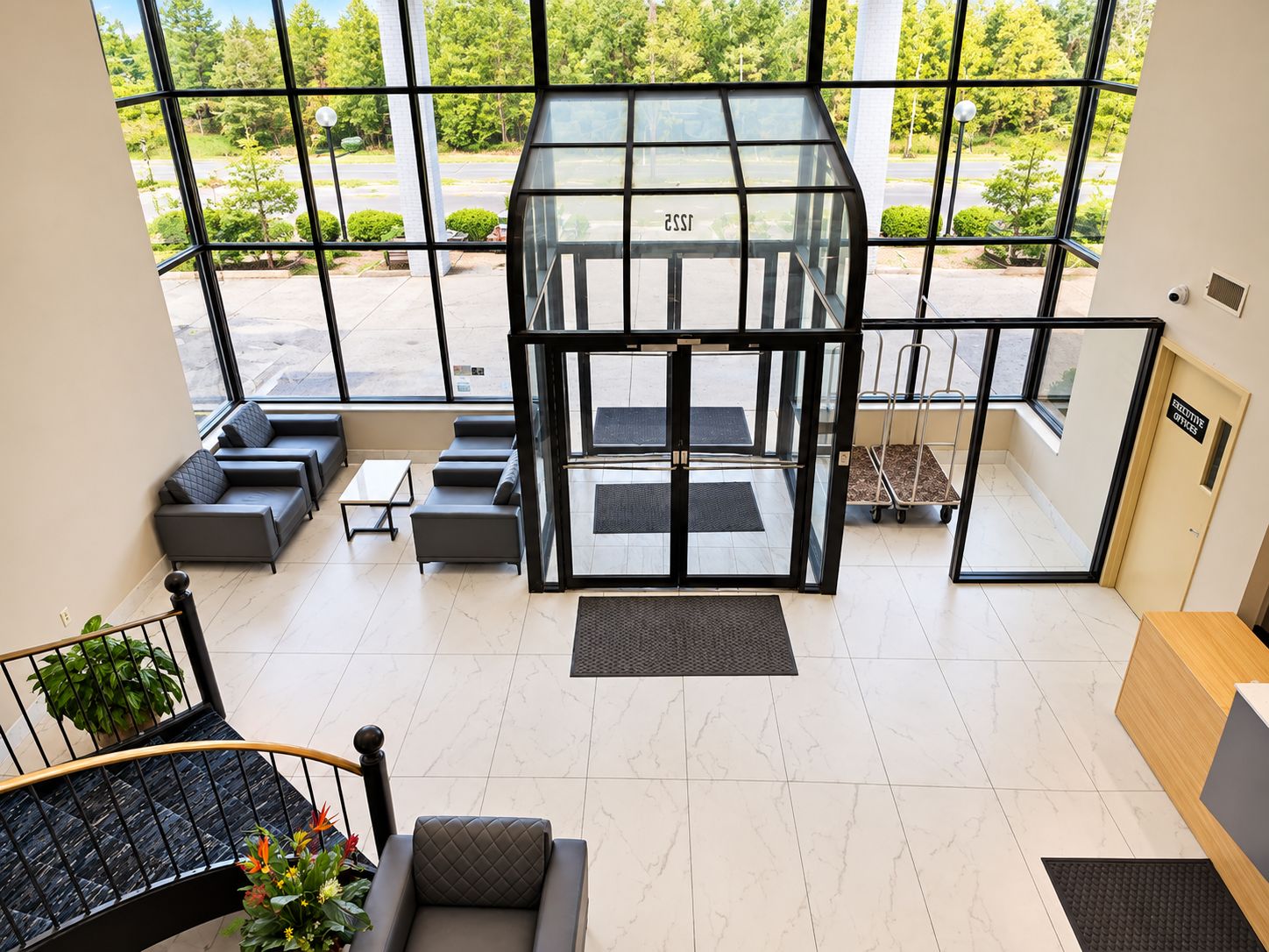 A modern lobby with a glass elevator, seating area, and a staircase with a railing.