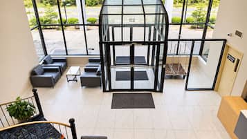A modern lobby with a glass elevator, seating area, and a staircase with a railing.