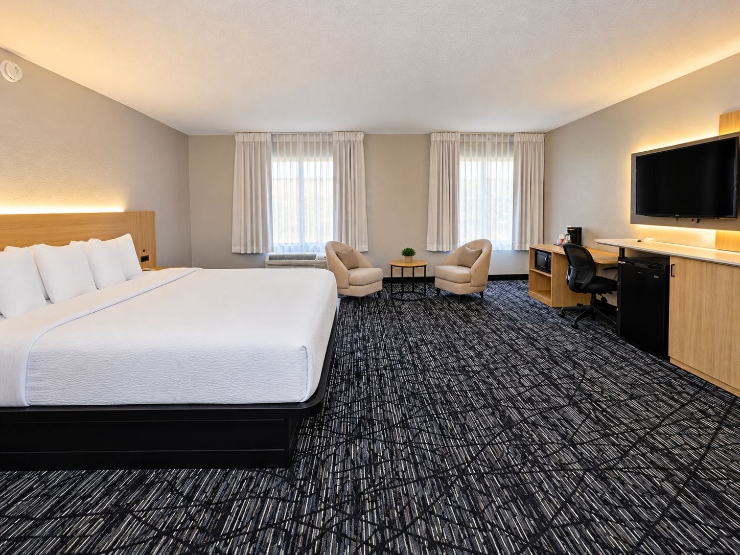 Una habitación de hotel con una cama grande, dos sillones, un escritorio con televisor y un minibar.