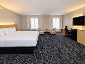 Una habitación de hotel con una cama grande, dos sillones, un escritorio con televisor y un minibar.