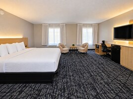 Una habitación de hotel con una cama grande, dos sillones, un escritorio con televisor y un minibar.