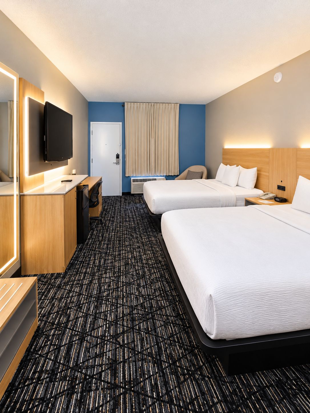 A hotel room with two beds, a desk, a chair, a television, and a door.