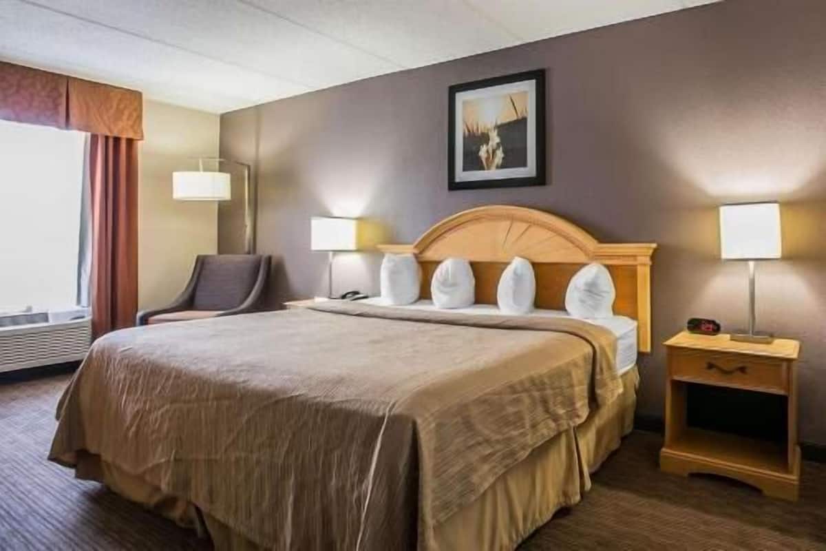 Ein Hotelzimmer mit einem großen Bett, einem Sessel, einem Nachttisch und einem Bild an der Wand.