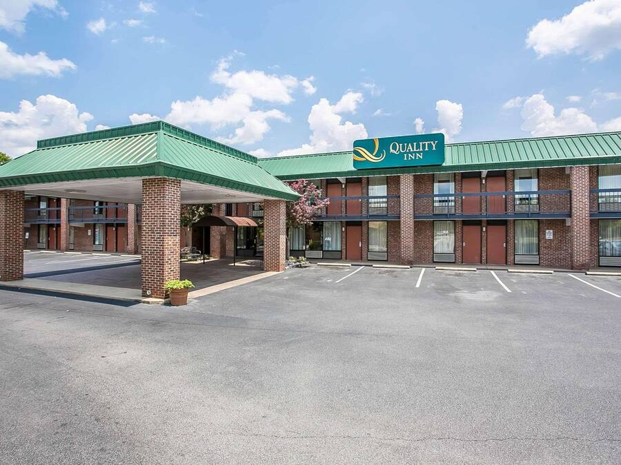 Un Quality Inn con fachada de ladrillo, techo verde y zona de estacionamiento cubierta.