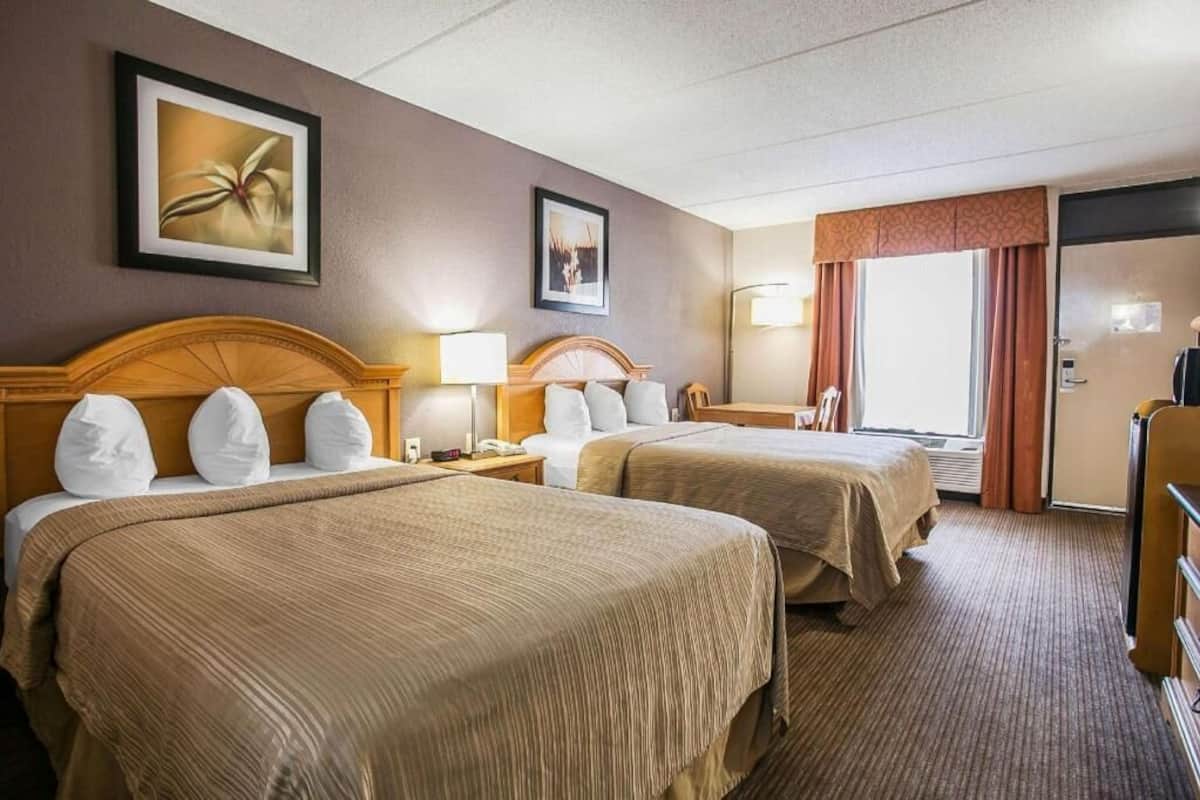 Ein Hotelzimmer mit zwei Betten, einem Schreibtisch, einem Stuhl, einer Lampe und einer Tür.