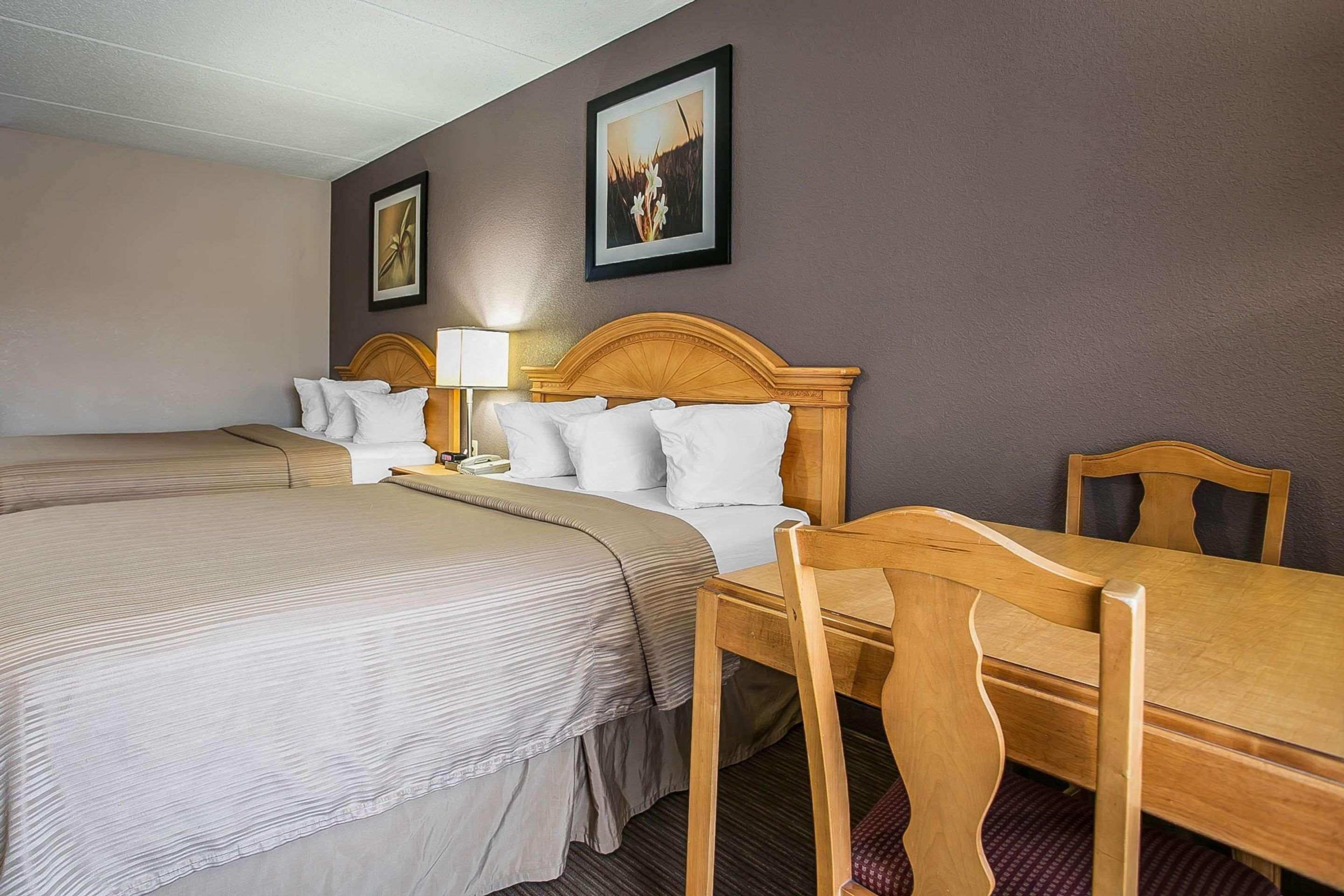 Quarto de hotel com duas camas, uma mesa de madeira e uma cadeira.