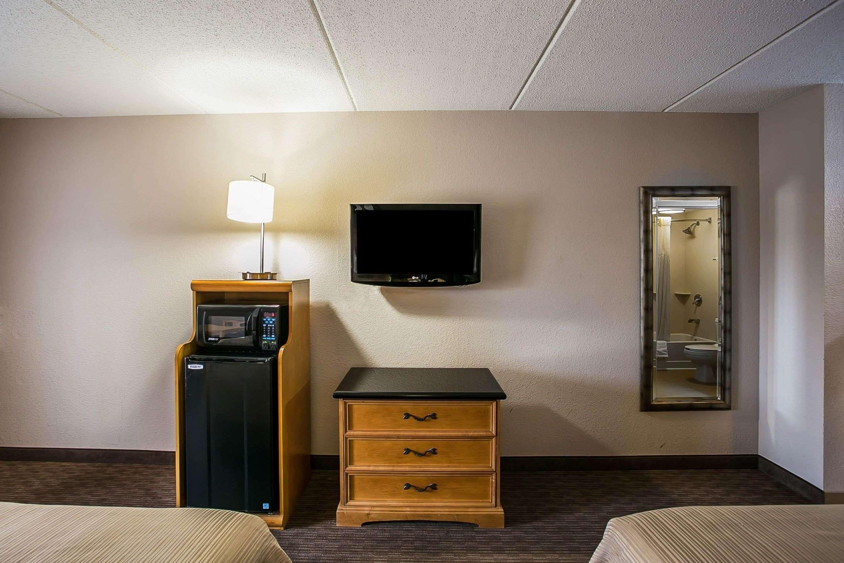 Una habitación de hotel con una cama, un escritorio con lámpara, un televisor y un espejo.