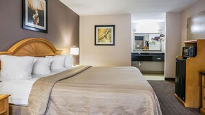 A hotel room with a bed, a wooden headboard, a bedside table, a lamp, a framed picture on the wall, a small kitchenette with a microwave, and a refrigerator. - Quality Inn Hartsville (Hartsville)
