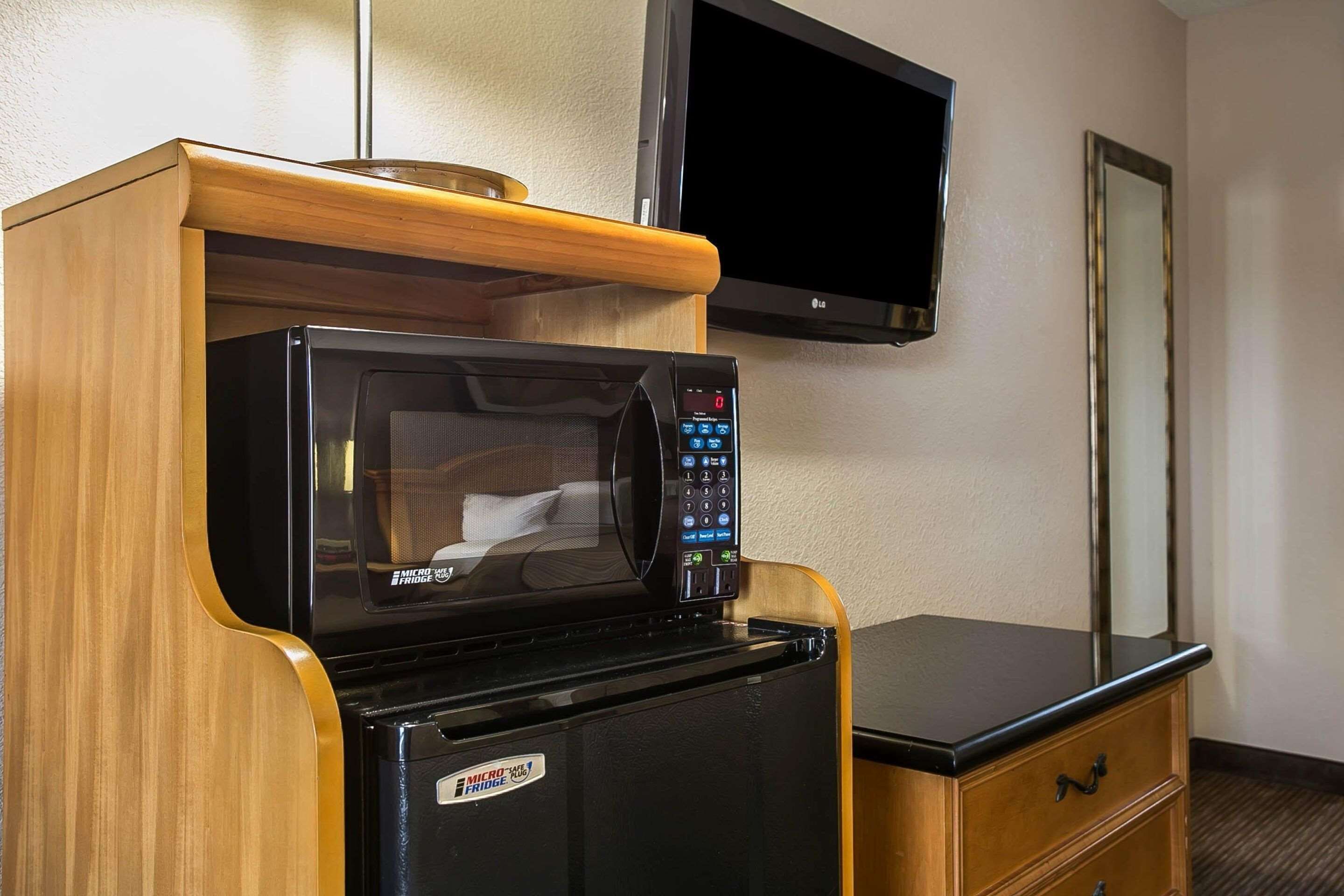 Una kitchenette compacta con microondas y refrigerador, un armario de madera, un televisor de pantalla plana y un espejo.