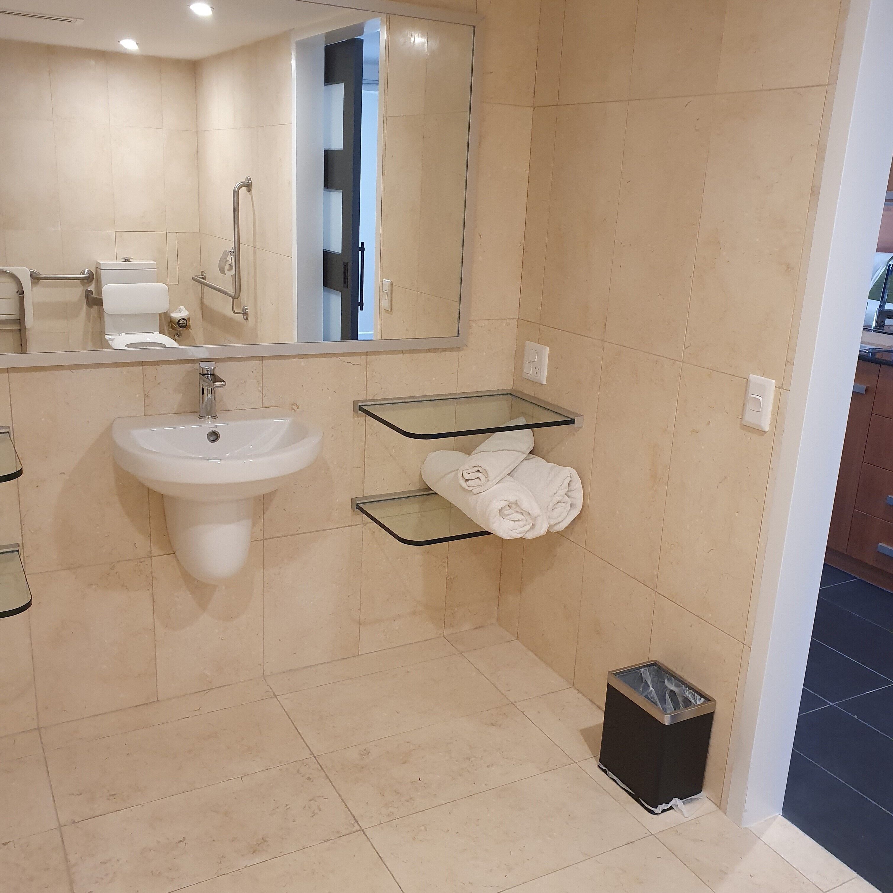 Une salle de bain équipée d’un lavabo, d’un miroir, d’un porte-serviettes et d’une poubelle.