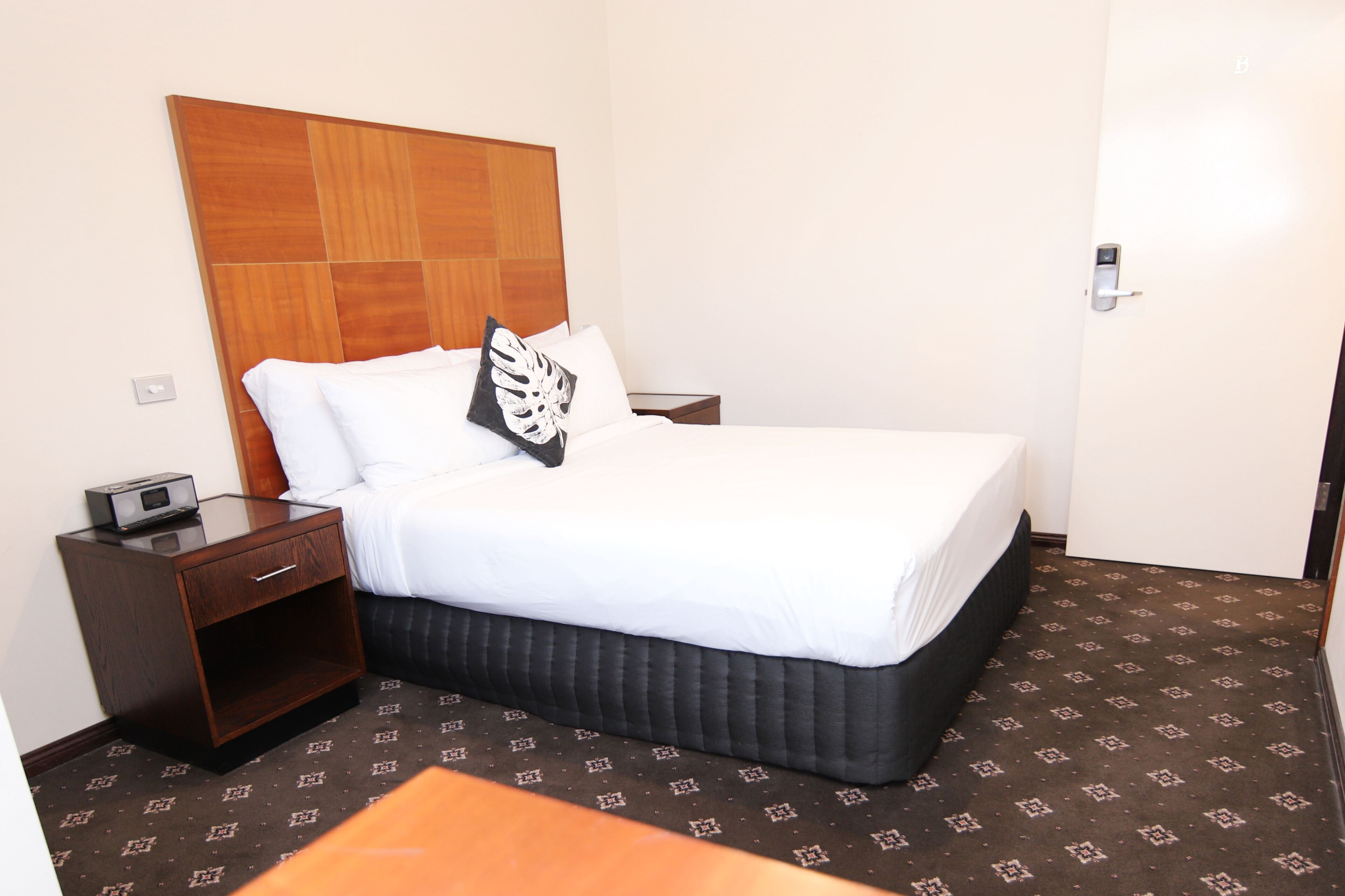 Ein Hotelzimmer mit einem großen Bett, einem Holzkopfende, einem Nachttisch mit Lampe und einem gemusterten Teppich.