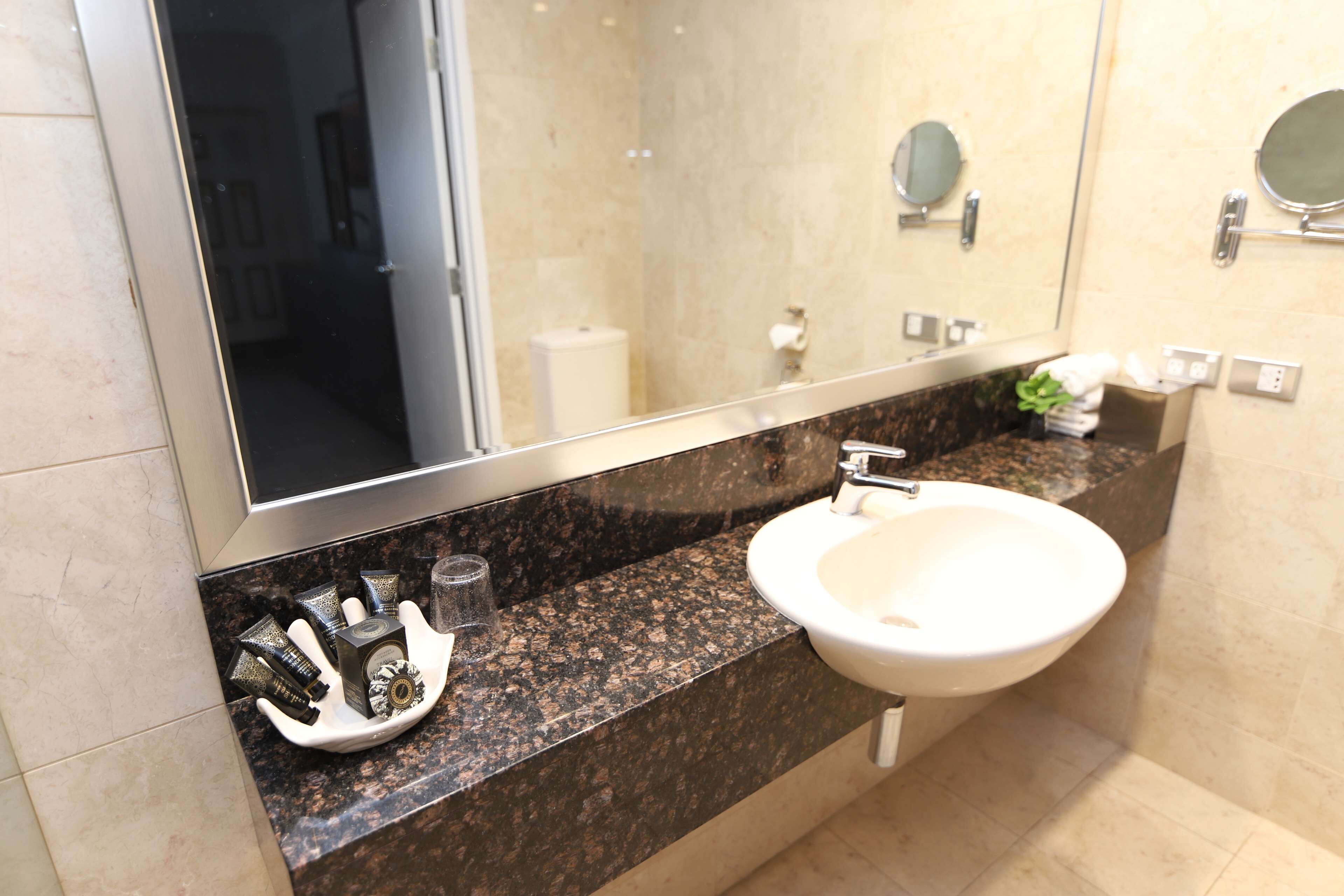Une salle de bain avec un lavabo blanc, un comptoir en granit et un grand miroir.