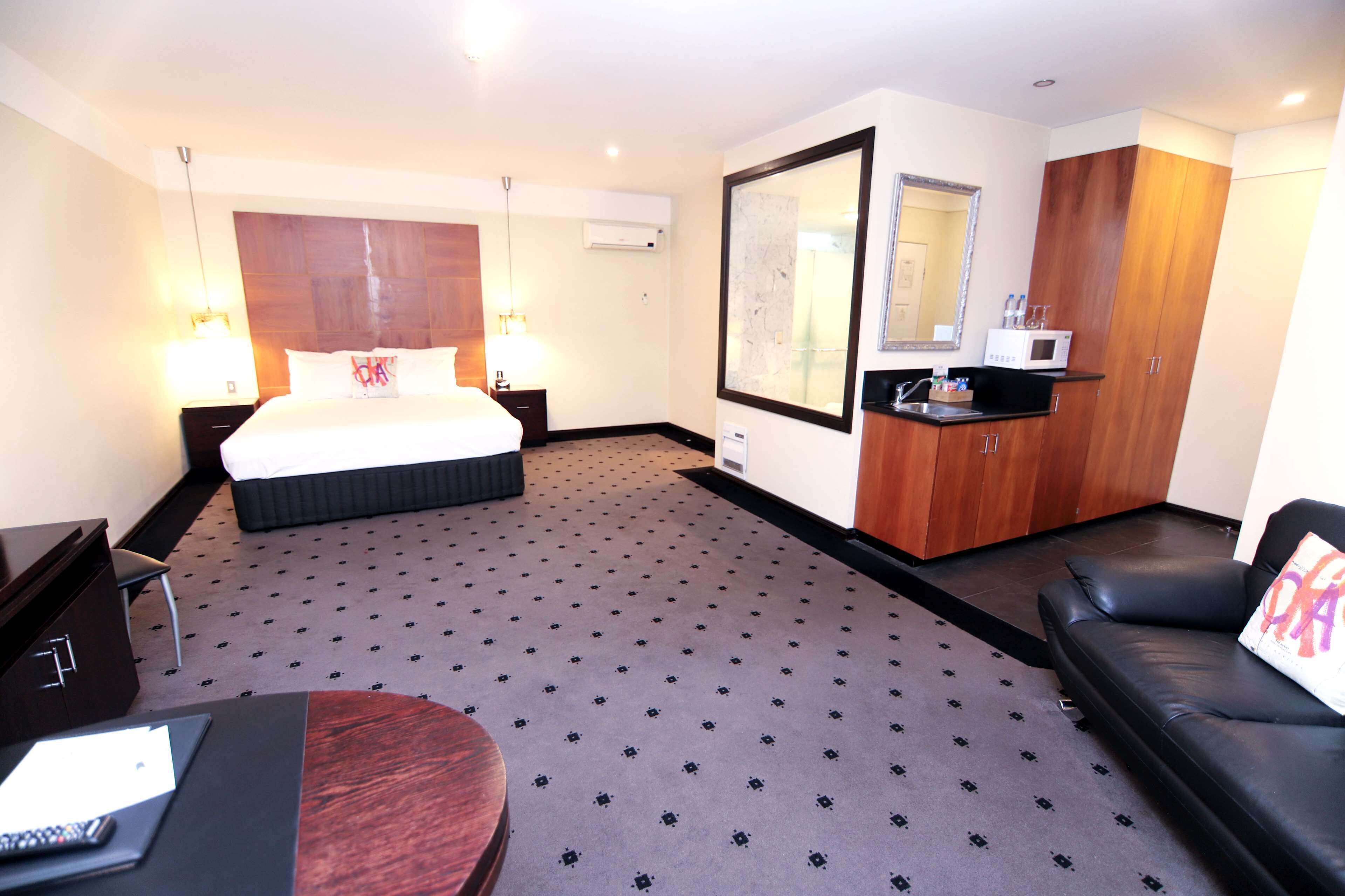 Une chambre d’hôtel comprenant un lit, un bureau, un canapé, un miroir et une kitchenette.