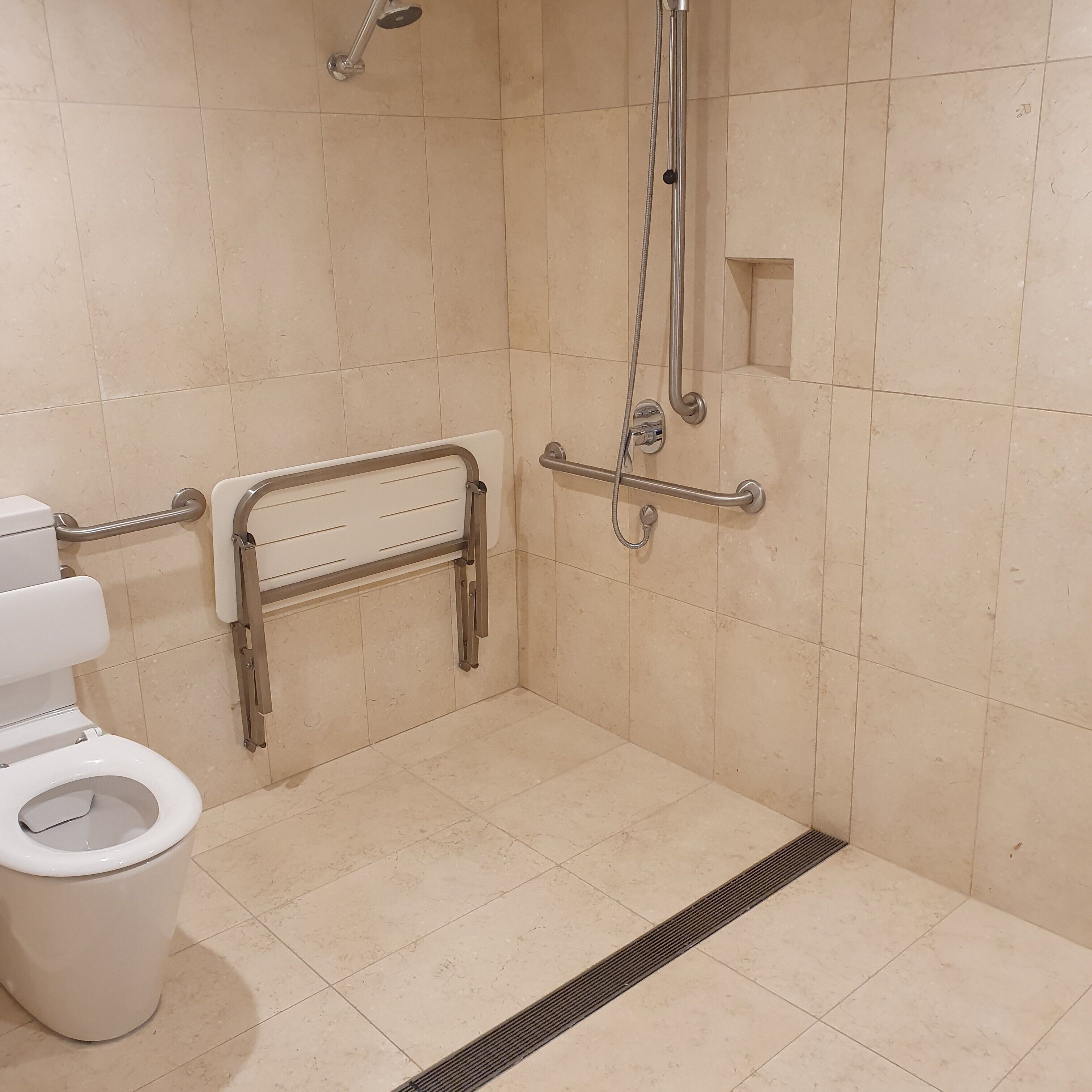 A bathroom with a toilet, grab bars, a shower with a handheld showerhead, and a floor drain.
