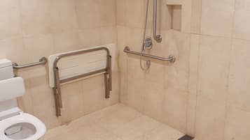 A bathroom with a toilet, grab bars, a shower with a handheld showerhead, and a floor drain.