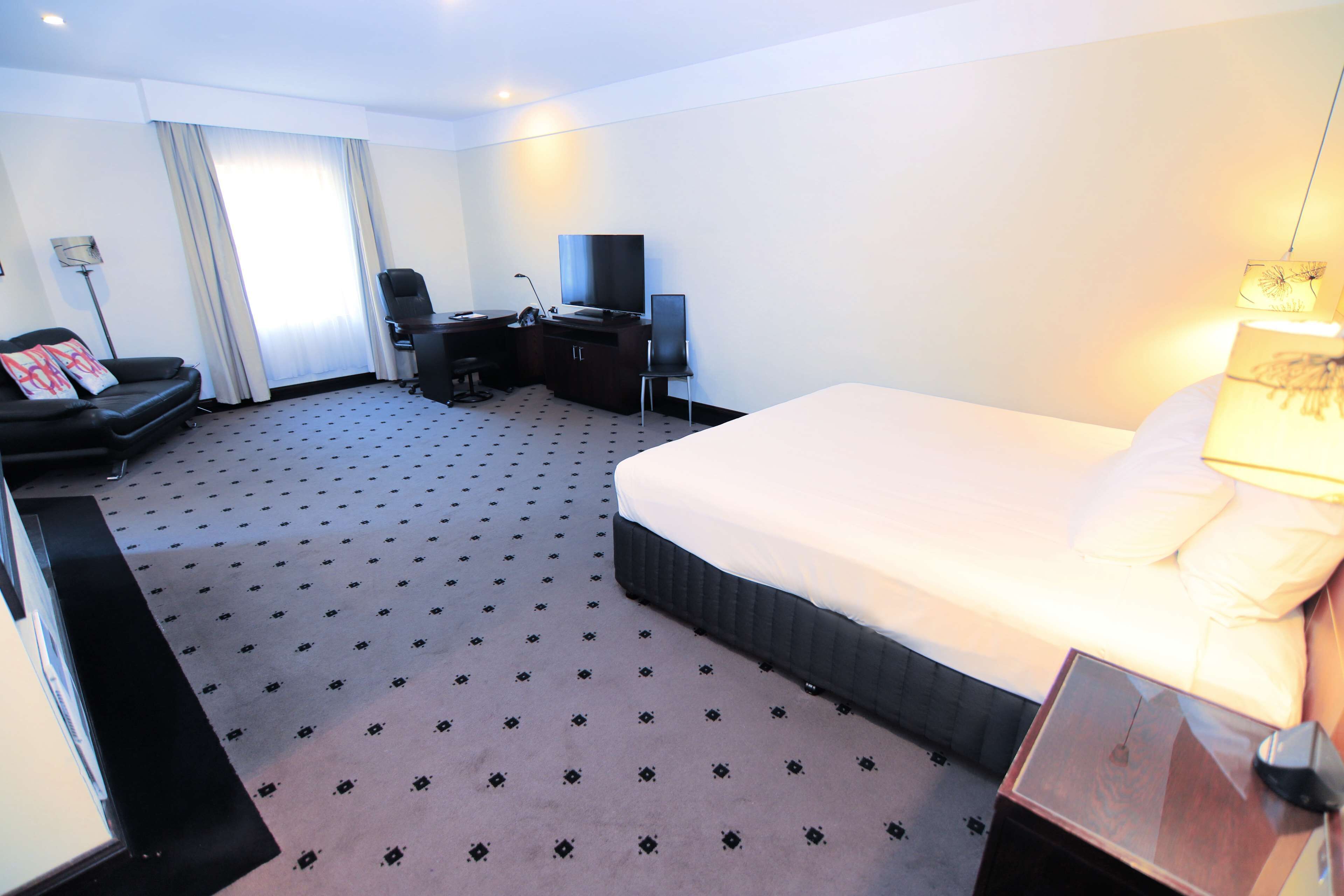 A hotel room with a large bed, a desk with a chair, a television, and a lamp.