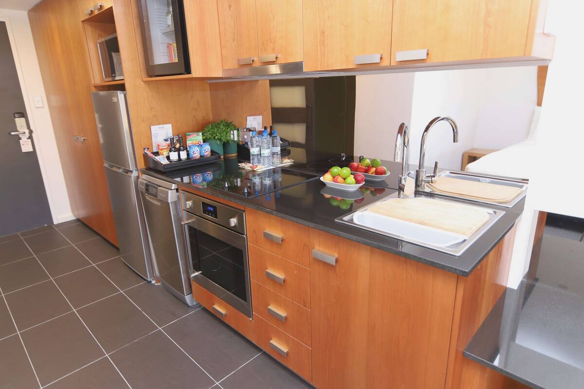 A modern kitchen with wooden cabinets, stainless steel appliances, and a black countertop.