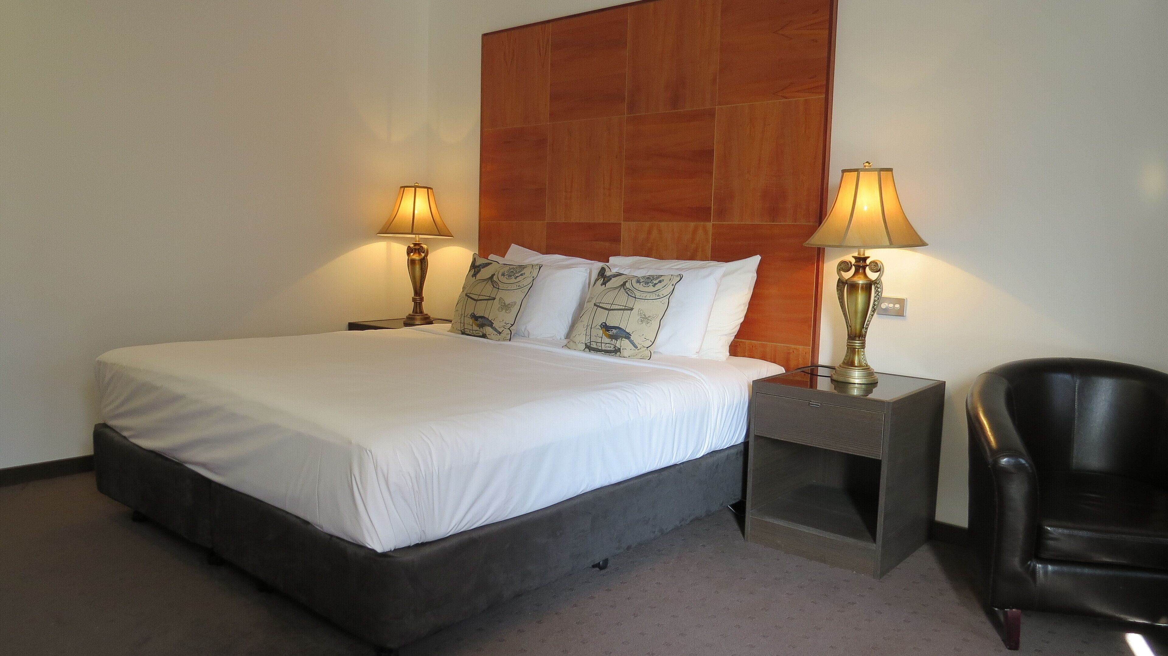 Habitación de hotel con una cama grande, dos lámparas de noche, una silla y un cabecero de madera.
