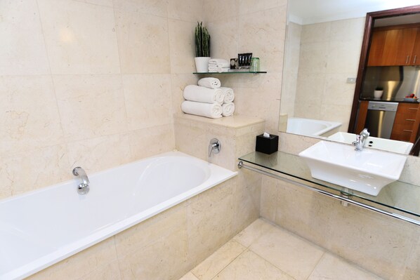 A modern bathroom with a glass-enclosed bathtub, a glass vanity with a sink, and a mirror above the sink. There are towels and toiletries on a shelf above the bathtub. - Best Western Plus Goulburn (Goulburn)