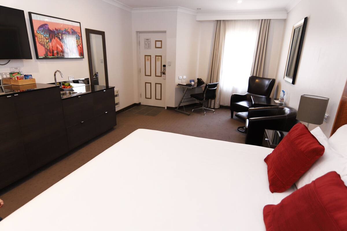 A hotel room with a bed, a desk, a chair, a dresser, and a TV on the wall.