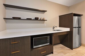 A kitchen with a built-in microwave, a stainless steel refrigerator, wooden cabinets, and a white countertop. - Hotel Indigo Rochester – Mayo Clinic Area by IHG (Rochester)