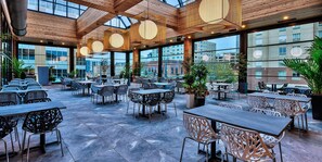 A spacious outdoor dining area with modern furniture and large windows offering views of the city.